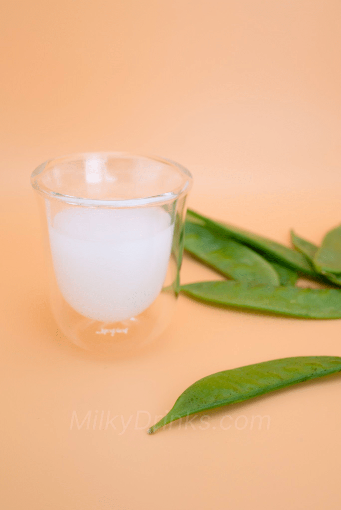 Calpico White Peach drink in a clear espresso glass with snow peas in frame and on a peach background
