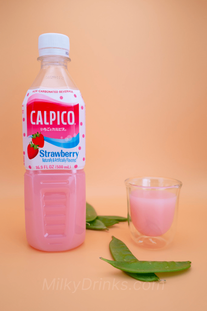 Calpico Strawberry drink plastic bottle next to a glass of Calpico Strawberry with snow peas in foreground and background, and on a peach background