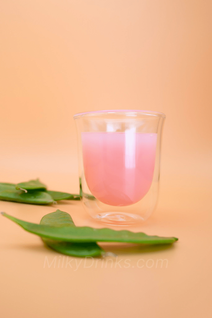 Calpico Strawberry in a transparent espresso glass with snow peas in foreground and background, on a peach colored background