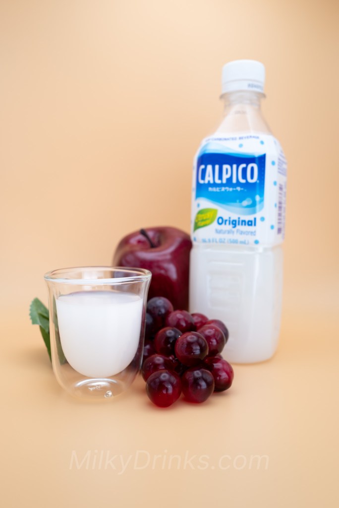 Calpico Original / Calpis Water bottle and also poured into a transparent espresso cup with fruit on a peach background