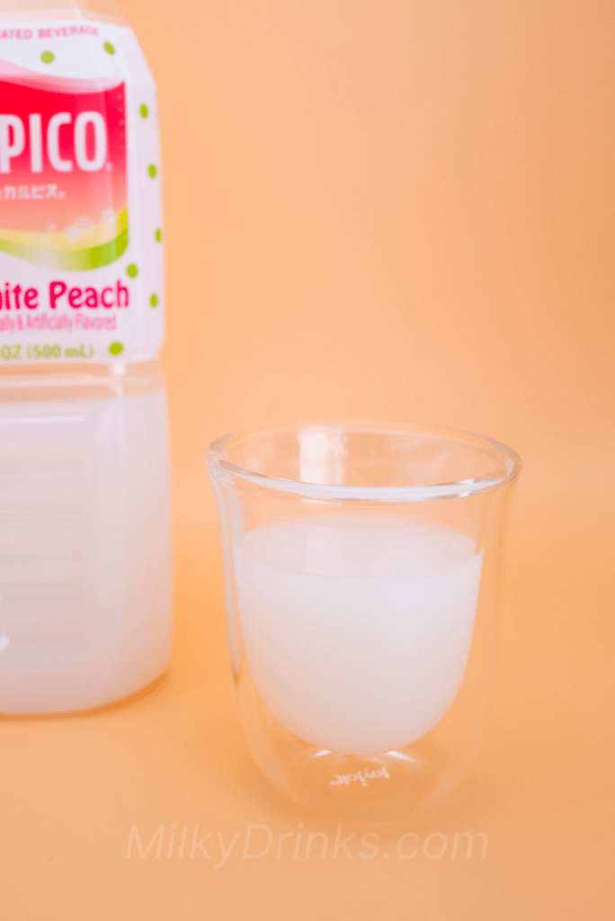 Calpico White Peach in a transparent espresso glass with the bottled drink in the background, and on a peach background