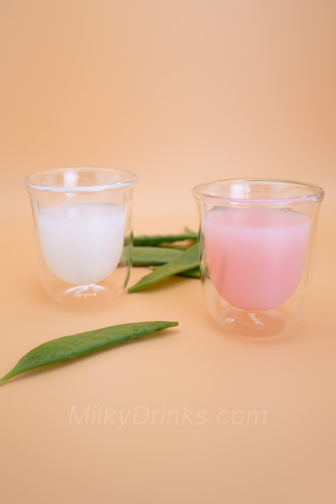 Calpico White Peach and Calpico Strawberry in transparent espresso glasses on a peach background, with snow peas in foreground