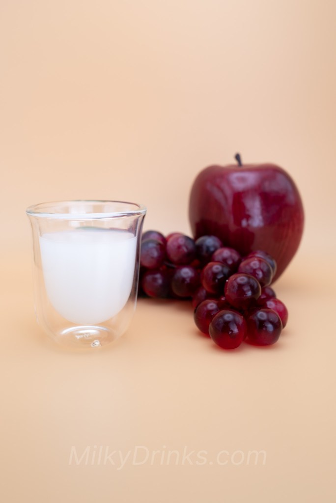 Calpico Original / Calpis Water in a transparent espresso glass with an apple and grapes, on a peach background